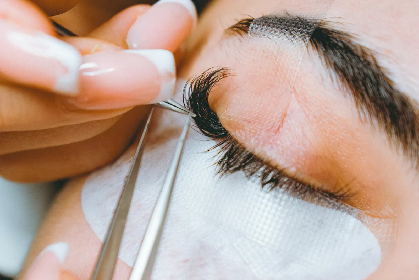 Close-up of a lash artist placing an extension with fine tweezers.